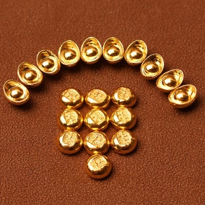 May include: Arrangement of small, gold-colored ingots and round, coin-like objects on a brown surface. The ingots are arranged in an arch, while the coins form a square below. The objects have a shiny, reflective surface.