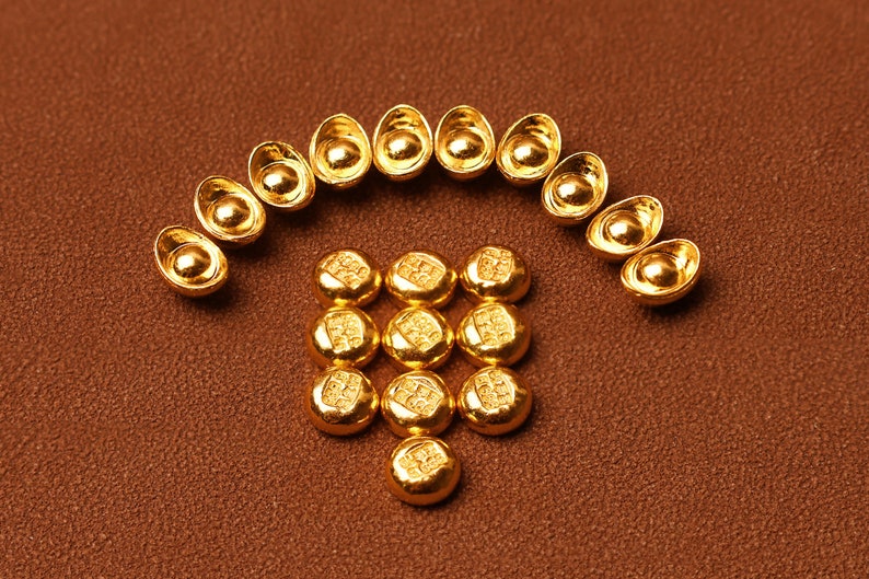May include: Arrangement of small, gold-colored ingots and round, coin-like objects on a brown surface. The ingots are arranged in an arch, while the coins form a square below. The objects have a shiny, reflective surface.