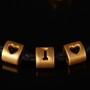 May include: A black leather bracelet with gold beads that spell out "I love you".