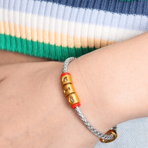 May include: A silver braided bracelet with a gold charm that says "GIG" in red and gold letters.