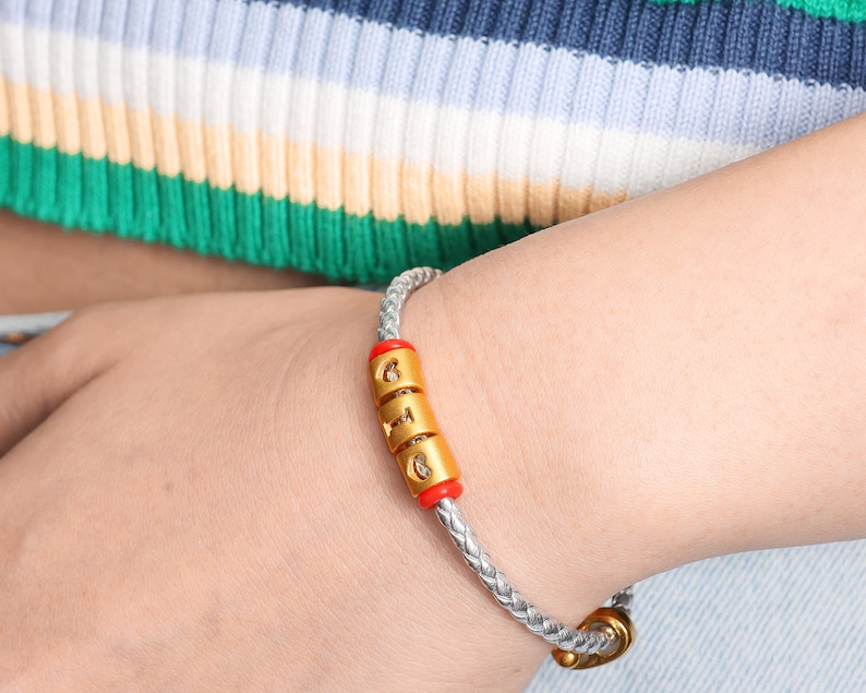 May include: A silver braided bracelet with a gold charm that says "GIG" in red and gold letters.
