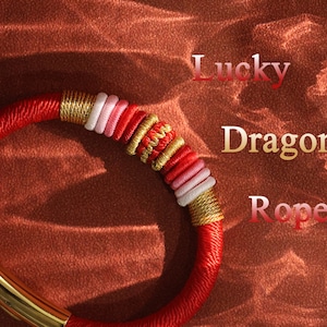 Puede incluir: Pulsera de cuerda trenzada roja, blanca y dorada con las palabras "Lucky Dragon Rope" sobre un fondo marrón.