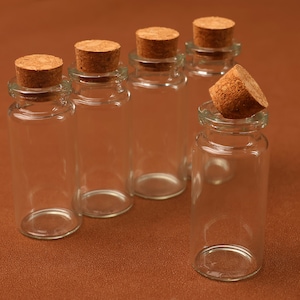 May include: Clear glass bottles with cork stoppers. The bottles are cylindrical with a narrow neck and a wider base. The corks are a light brown color. One cork is removed from its bottle. The background is a solid brown color.