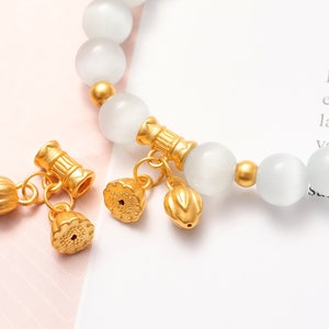 May include: A white gemstone bracelet with gold accents and charms. The charms are shaped like lotus flowers and have a detailed design.