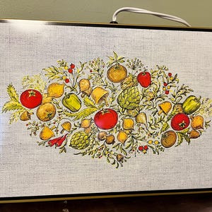 Puede incluir: Luminaria rectangular con una superficie texturizada de lino, que presenta una colorida ilustración de varias verduras y hierbas. El diseño incluye tomates, pimientos, alcachofas y champiñones. La luminaria tiene un marco marrón oscuro y un cable blanco.