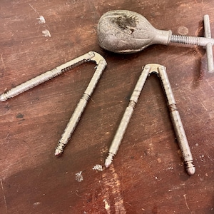 Puede incluir: Un surtido de cascanueces antiguos y una herramienta para cascar nueces. Los cascanueces son de color plateado con patrones detallados. La herramienta tiene una cabeza bulbosa y un mecanismo de tornillo. Están colocados sobre una superficie de madera.