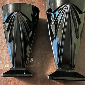 May include: Two black glass cups with a geometric design. The cups have a wide base and a narrow top.