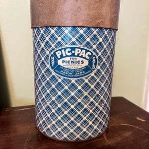 Puede incluir: Contenedor aislado vintage para picnics. El recipiente cilíndrico presenta un patrón de diamantes azules y blancos. El texto "PIC-PAC for PICNICS" se muestra en la parte delantera. Diseñado para mantener los tarros Mason calientes o fríos durante varias horas.