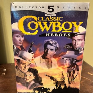 May include: A DVD box set titled "Classic Cowboy Heroes", featuring a 5-pack collector's series. The cover displays images of actors in cowboy attire, with the title in yellow. The background has a sunset colour scheme.
