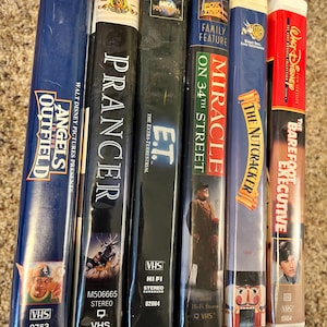 Könnte beinhalten: Eine Reihe von sechs VHS-Kassetten mit verschiedenen Filmtiteln, darunter "Angels in the Outfield", "Prancer", "E.T. der Außerirdische", "Wunder in Manhattan", "Der Nussknacker" und "Der Barfuß-Manager".