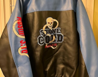 May include: A blue and black faux leather varsity jacket featuring an embroidered skull and snake graphic on the back with the text "STONE COLD" and "Austin 3:16". The sleeves are blue with red text and snake embroidery, and the collar and cuffs are striped.