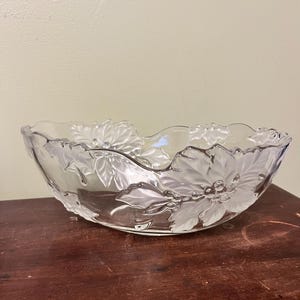 Puede incluir: Cuenco de vidrio transparente con diseños de flores de pascua esmeriladas alrededor del borde. El cuenco tiene un borde festoneado y está sobre una superficie de madera oscura. Las flores de pascua tienen hojas y bayas detalladas.