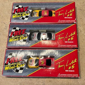 Op de afbeelding: Drie dozen met verzamelbare miniatuur-auto's met Terry Labonte, de NASCAR Winston Cup Series Champion van 1996. Elke doos heeft een rode en gele auto met nummer 5 en sponsoring van Kellogg's. De dozen hebben een rode achtergrond met de tekst "FREE Collectible Die-Cast Mini-Car" en "Terry Labonte #5 1996 Champion".