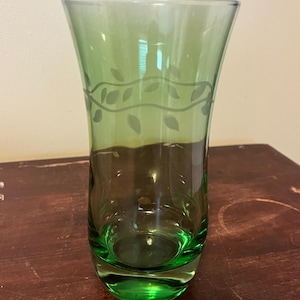 May include: A green glass vase with a vine and leaf design etched into the side.