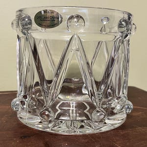 以下が含まれることがあります： 幾何学模様の透明クリスタルガラス。ガラスは円筒形で、広い開口部があり、球状のアクセントで飾られています。「24% Lead Crystal Fine Bohemian Crystal」と書かれたラベルが付いています。