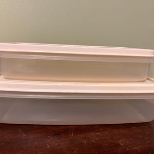 May include: Two rectangular food storage containers stacked on top of each other. Each container is made of translucent, frosted plastic and features a solid, light beige lid that fits securely over the top edge of the container base.