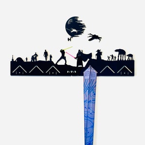May include: Black metal wall mount shaped like a Star Wars scene with a Death Star, TIE fighter, and characters from the movie. A blue and silver medal is hanging from the mount.