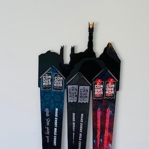 May include: Four black and red running race medals with the text "The Conquer ROR" and "Make Every Mile Count" hanging on a black metal silhouette of the tower of Barad-dûr from the Lord of the Rings.