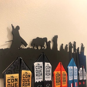 May include: Black metal medal display rack with a silhouette of characters from the Lord of the Rings. The rack has eight slots for medals. The medals are colorful and have the text "The Conqueror" on them.