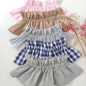 Op de afbeelding: Een collectie van vijf stoffen kragen met geplooide randen, voorzien van diverse patronen waaronder roze strepen, beige stippen, blauw-witte krijtstrepen, blauw-wit gingham ruitpatroon en grijze krijtstrepen, gerangschikt in een verticale stapel.