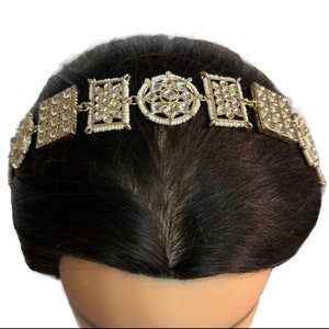 May include: A gold headband with a decorative design featuring clear rhinestones and a central circular motif. The headband is worn on a model with dark brown hair.