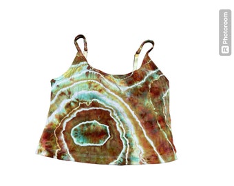 Pode incluir: Um top de tanque tie-dye com um padrão de redemoinho marrom, verde e branco. O top tem alças finas e um decote redondo.