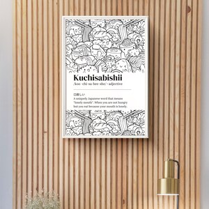 May include: A framed monochrome print featuring the word "Kuchisabishii" and its phonetic spelling. The print has a doodle-style illustration of food and characters. The definition of the Japanese word is also included.