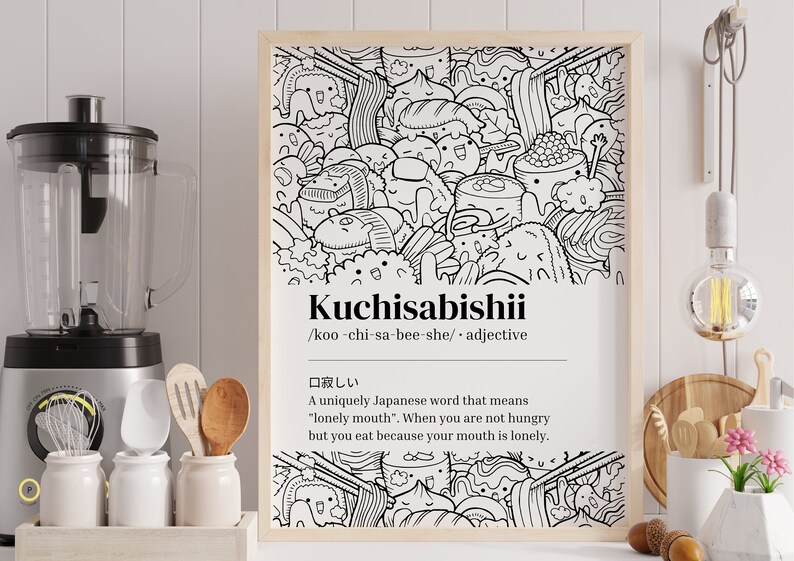 May include: A framed monochrome print displaying the Japanese word "Kuchisabishii" and its definition. The illustration depicts a playful assortment of food items, including sushi and ramen, with cartoon-style faces.