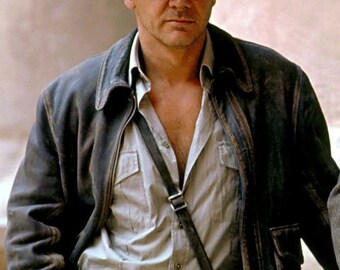 Puede incluir: Un hombre con una chaqueta de cuero marrón, un fedora marrón claro, una camisa de botones gris claro y un cinturón marrón con una hebilla dorada.