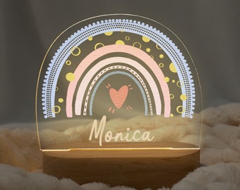 Puede incluir: Una luz nocturna con forma de arcoíris con un corazón y lunares. La luz está sobre una base de madera y el nombre "Monica" está escrito debajo del arcoíris.