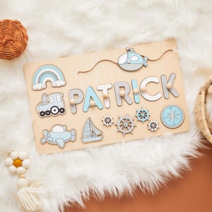 May include: Wooden name puzzle with the name "PATRICK" in light blue and gray letters. The puzzle features a rainbow, train, airplane, sailboat, submarine, compass, and ship wheels. The puzzle is made of light-colored wood.