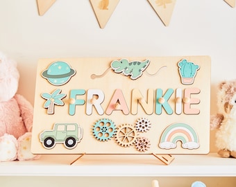 May include: A wooden personalized name puzzle with the name Frankie. The puzzle features a variety of colorful shapes, including a dinosaur, a cactus, a palm tree, a jeep, gears, and a rainbow.