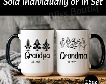 May include: Two white ceramic mugs with black handles and black rims. The mug on the left has a design of three trees and the text "Grandpa Est. 2025". The mug on the right has a design of flowers and the text "Grandma Est. 2025".