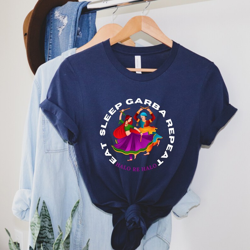 Puede incluir: Una camiseta azul marino con un gr&aacute;fico circular blanco que representa a dos personas bailando con el texto "Eat Sleep Garba Repeat Halo Re Halo".
