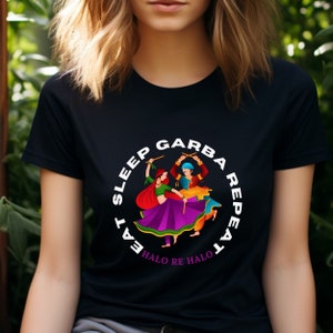 Puede incluir: Camiseta negra con un gr&aacute;fico circular blanco que muestra a dos personas bailando con ropa colorida. El texto alrededor del c&iacute;rculo dice "Eat Sleep Garba Repeat" y "Halo Re Halo".