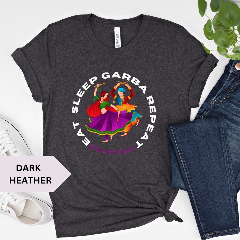 Puede incluir: Camiseta gris oscuro jaspeada con un gr&aacute;fico circular blanco que representa a una pareja bailando con palos. El texto alrededor del gr&aacute;fico dice "Eat Sleep Garba Repeat" con las palabras "Halo Re Halo" en la parte inferior.