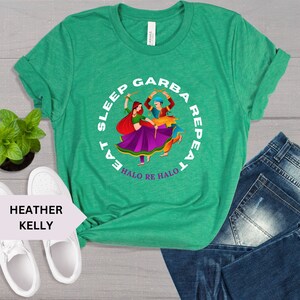 Puede incluir: Camiseta verde con un gr&aacute;fico circular blanco que representa a una pareja bailando con palos. El texto dentro del c&iacute;rculo dice "Eat Sleep Garba Repeat Halo Re Halo".