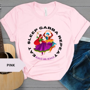 Puede incluir: Camiseta rosa con un gr&aacute;fico circular negro que representa a dos personas bailando con el texto "Eat Sleep Garba Repeat Halo Re Halo".