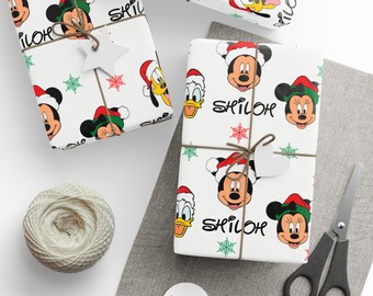 Puede incluir: Varios regalos envueltos con papel blanco con Mickey Mouse, Minnie Mouse, Donald Duck y Pluto con gorros de Papá Noel. Los regalos están atados con hilo y tienen etiquetas en forma de estrella.