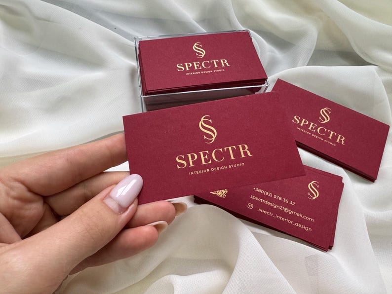 May include: Red business cards with gold lettering. The cards feature the logo "S" and the text "SPECTR INTERIOR DESIGN STUDIO". Contact information is included on the bottom of the card.