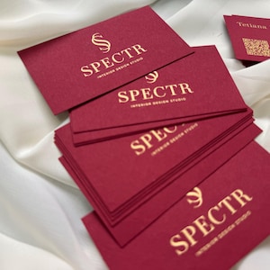 May include: A stack of red business cards with gold lettering. The text on the cards reads "SPECTR INTERIOR DESIGN STUDIO".