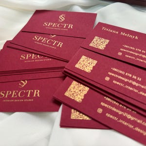 May include: A stack of burgundy business cards with gold lettering. The cards feature the logo "SPECTR Interior Design Studio" and contact information for Tetiana Melnyk, including a phone number, email address, and social media handle.