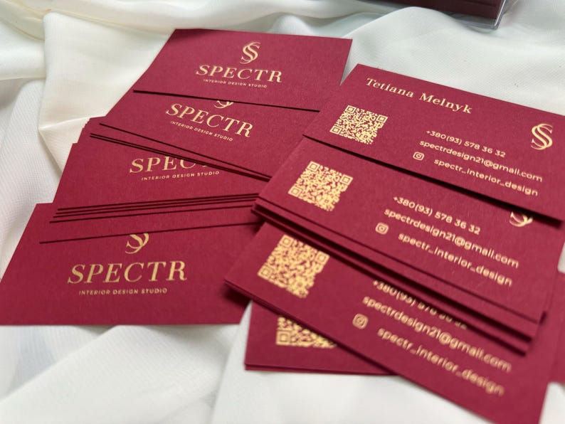 May include: A stack of burgundy business cards with gold lettering. The cards feature the logo "SPECTR Interior Design Studio" and contact information for Tetiana Melnyk, including a phone number, email address, and social media handle.