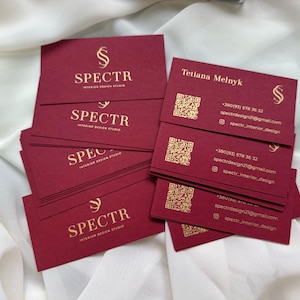 May include: A stack of burgundy business cards with gold lettering. The cards feature the logo "SPECTR Interior Design Studio" and contact information for Tetiana Melnyk, including a phone number, email address, and social media handle.