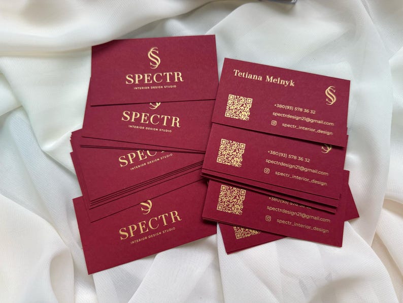May include: A stack of burgundy business cards with gold lettering. The cards feature the logo "SPECTR Interior Design Studio" and contact information for Tetiana Melnyk, including a phone number, email address, and social media handle.