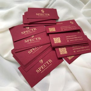 May include: A stack of burgundy business cards with gold lettering that reads "SPECTR Interior Design Studio".