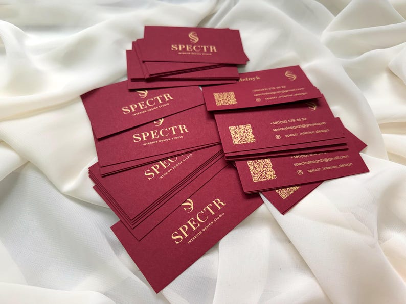 May include: A stack of burgundy business cards with gold lettering that reads "SPECTR Interior Design Studio".