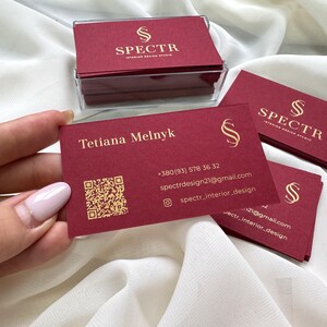 May include: Red business cards with gold lettering for SPECTR Interior Design Studio. The card includes the name Tetiana Melnyk, phone number, email address, and social media handle. A QR code is also included.