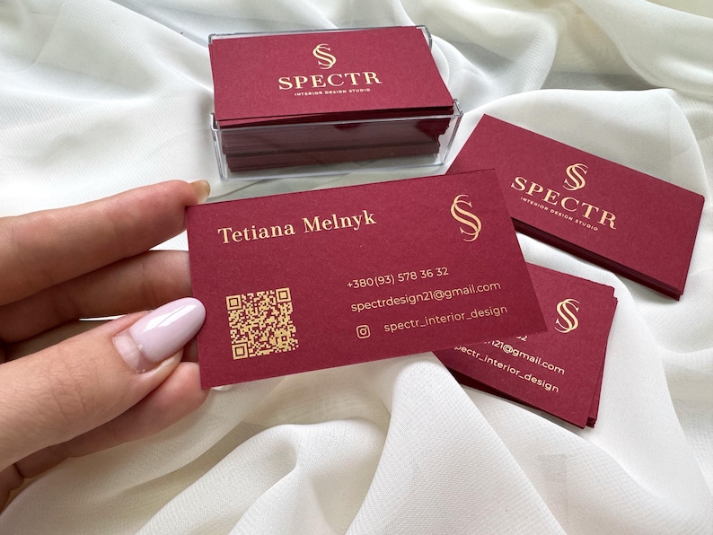 May include: Red business cards with gold lettering for SPECTR Interior Design Studio. The card includes the name Tetiana Melnyk, phone number, email address, and social media handle. A QR code is also included.
