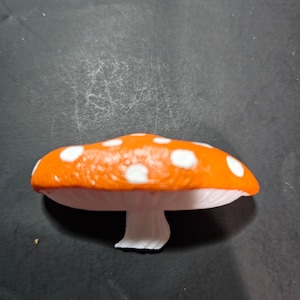 May include: Orange and white mushroom shaped figurine with white spots.